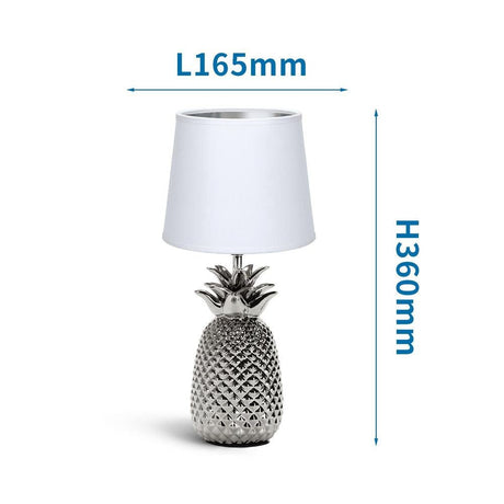 Moderne silberfarbene Tischlampe in Ananas-Optik mit weißem Stoffschirm.